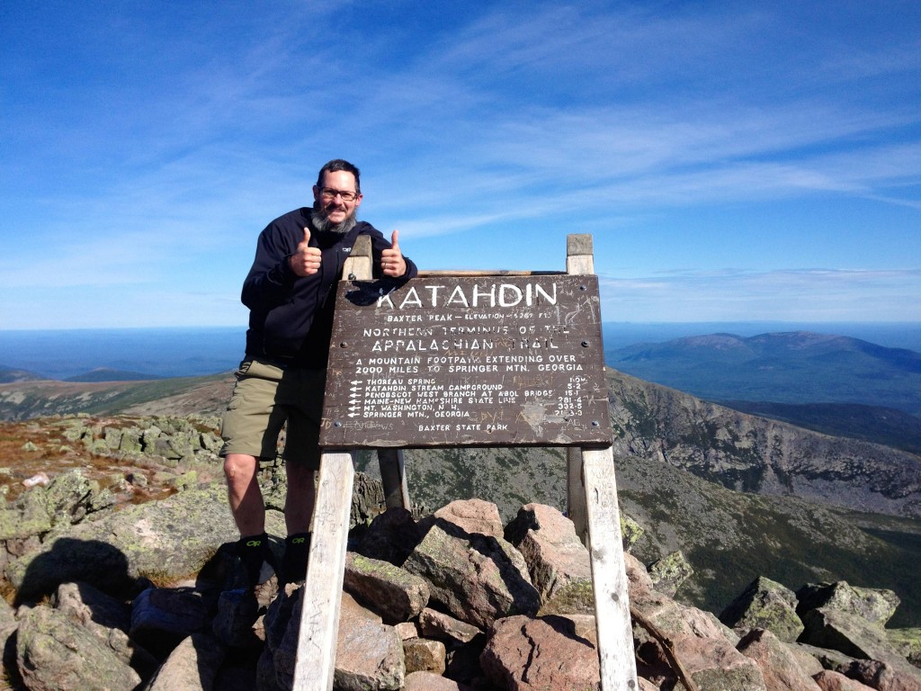 Appalachian Trail thru hiker slim jim aka chris spencer stands next to the sign at the peak of mount kathadin