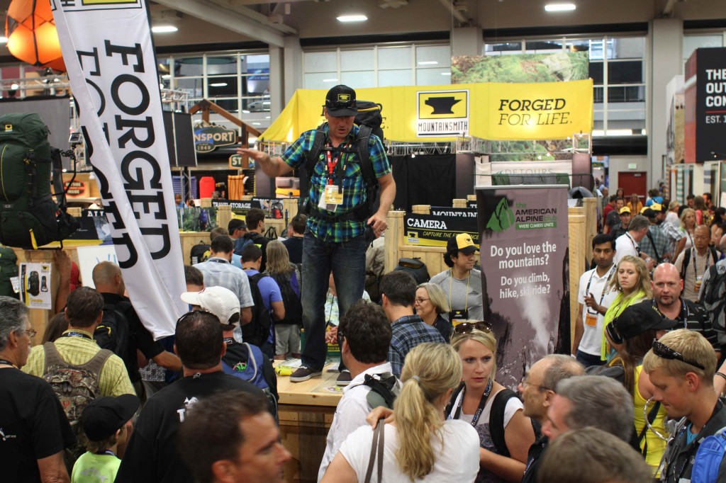 Andy Held of True Hero Events standing on the table at the mountainsmith booth at summer outdoor retailer