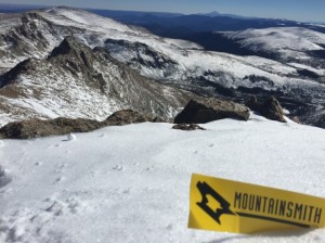 Mountainsmith logo in the snow with snowy mountain range in the background 