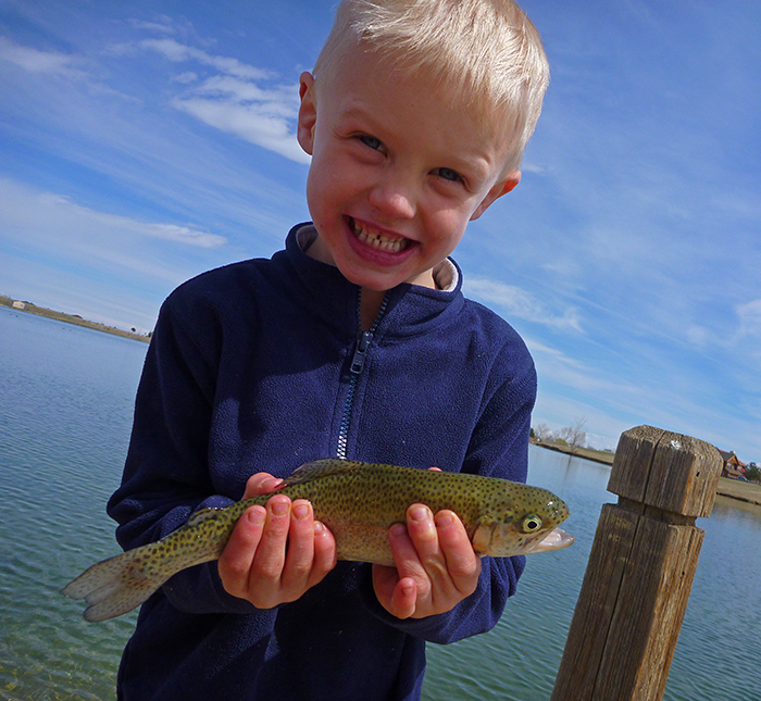 Kid with blue fleece jacket shown holding a trout on the river in Denver Colorado