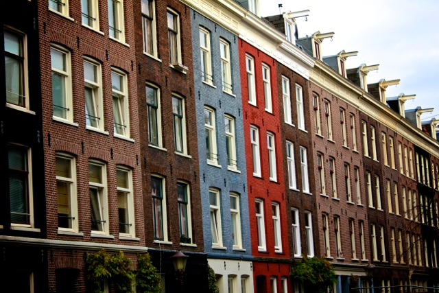 A red and blue house stick out in a row of houses in Amsterdam