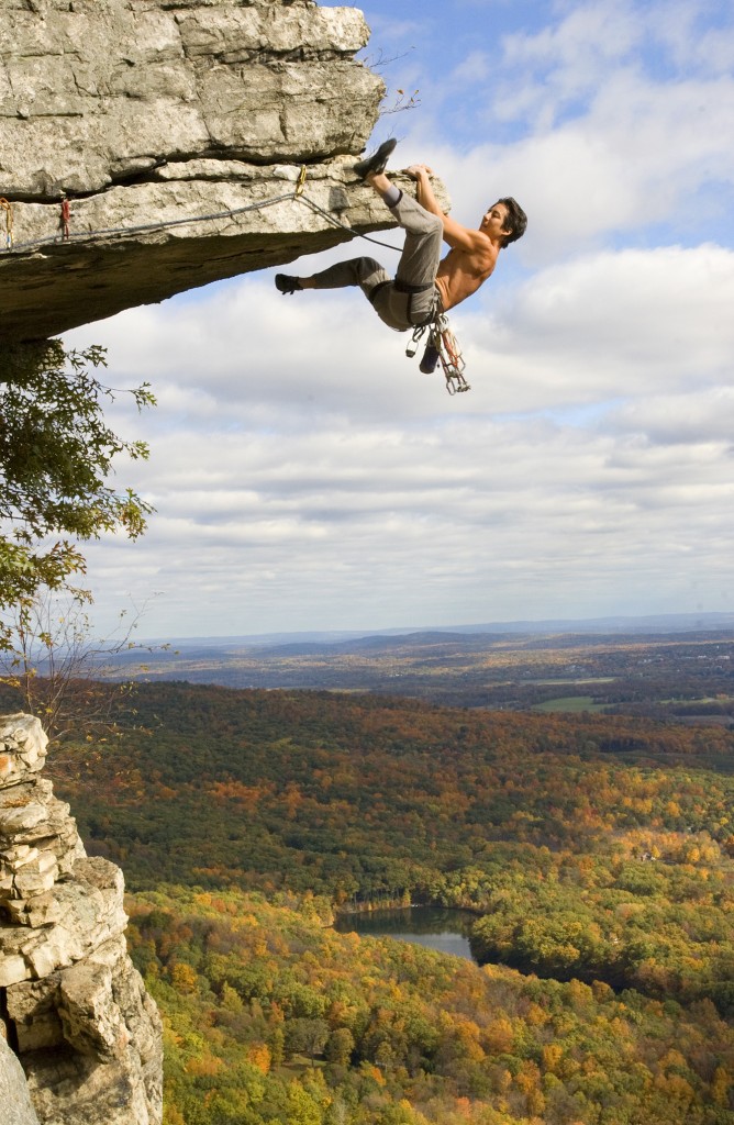 a climber swings his leg up over a rock on an overhang