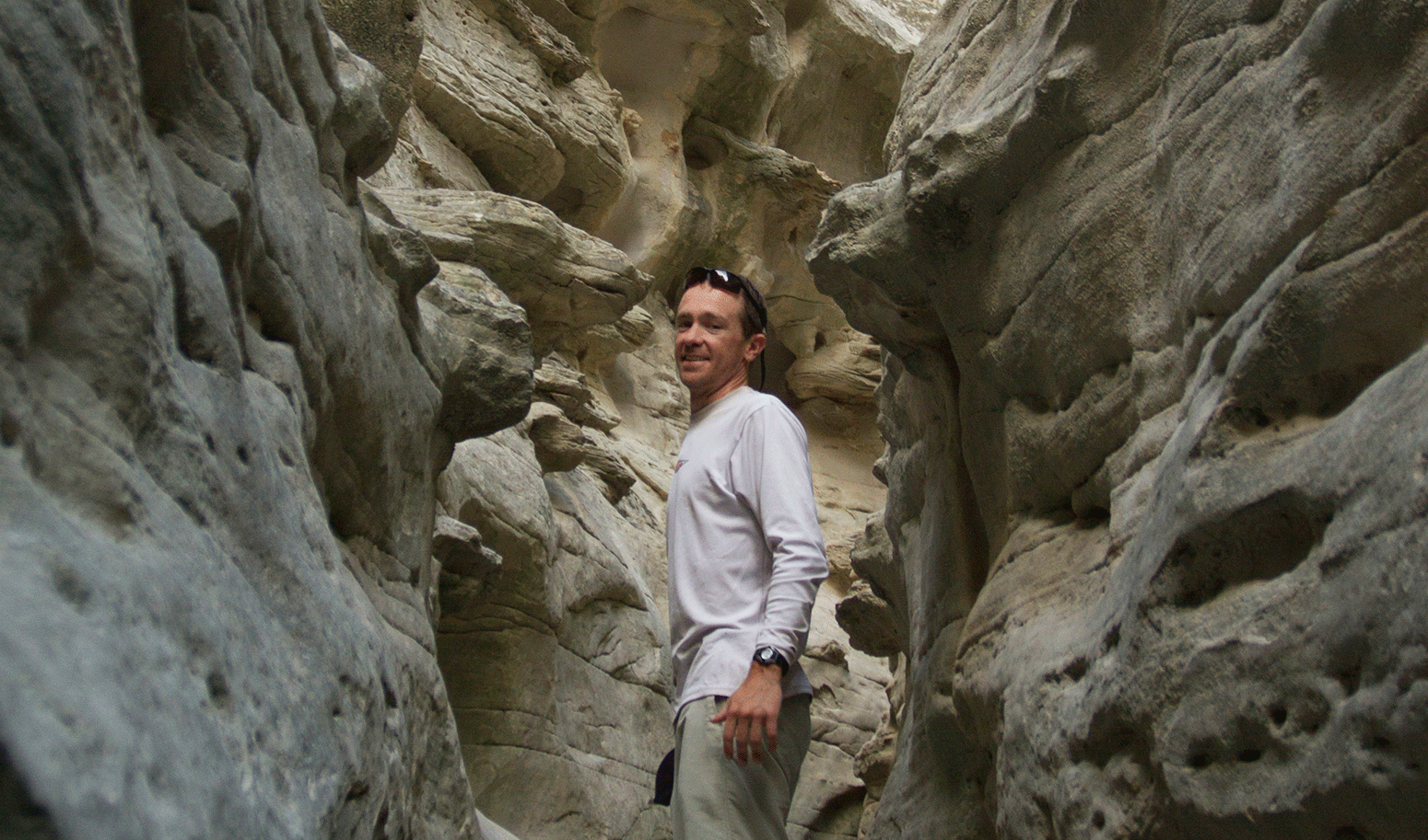 Joe Zimmermann, adventurer, idea man behind the Blackwater Drifters Expedition, and Mountainsmith Ambassador pictured hiking through a slot canyon in a white long sleeve shirt and khaki pants.