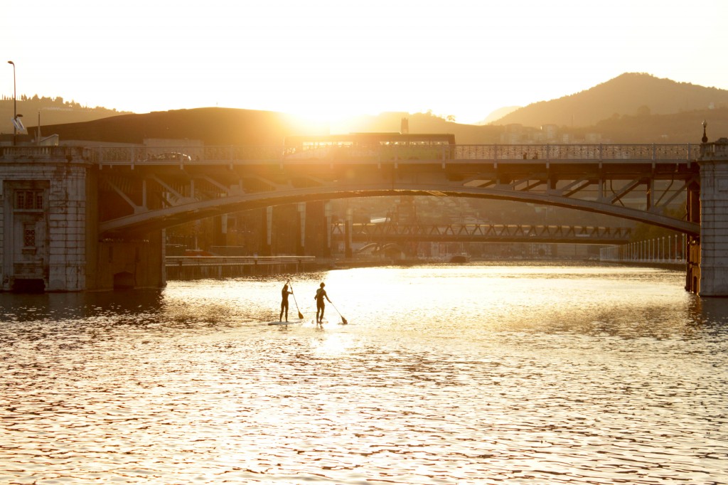 Two SUPers paddling down “La Ria” at sunset in Bilbao