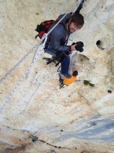 Andy Mann shooting photography while hanging off a rock wall with his Mountainsmith lumbar pack