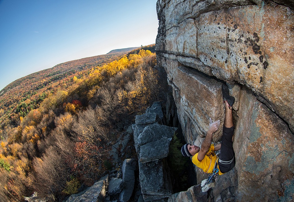 Rock climber toe hooking a hidden wall in New York with colorful autumn background. Catching the golden hour light 